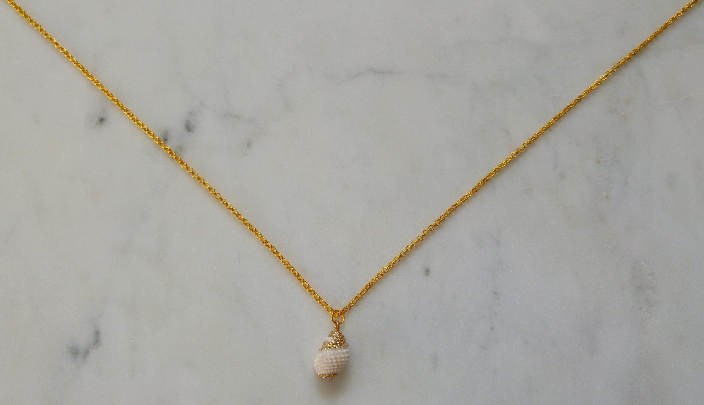 Guldfärgat halsband med en vit snäcka