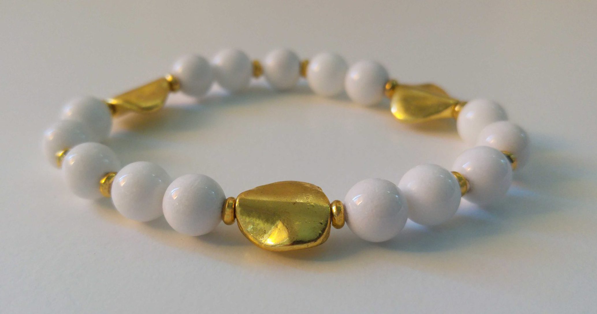 Elastiskt armband med vit jade, guldfärgade asymmetriska mellandelar och guldfärgade minirondeller.
